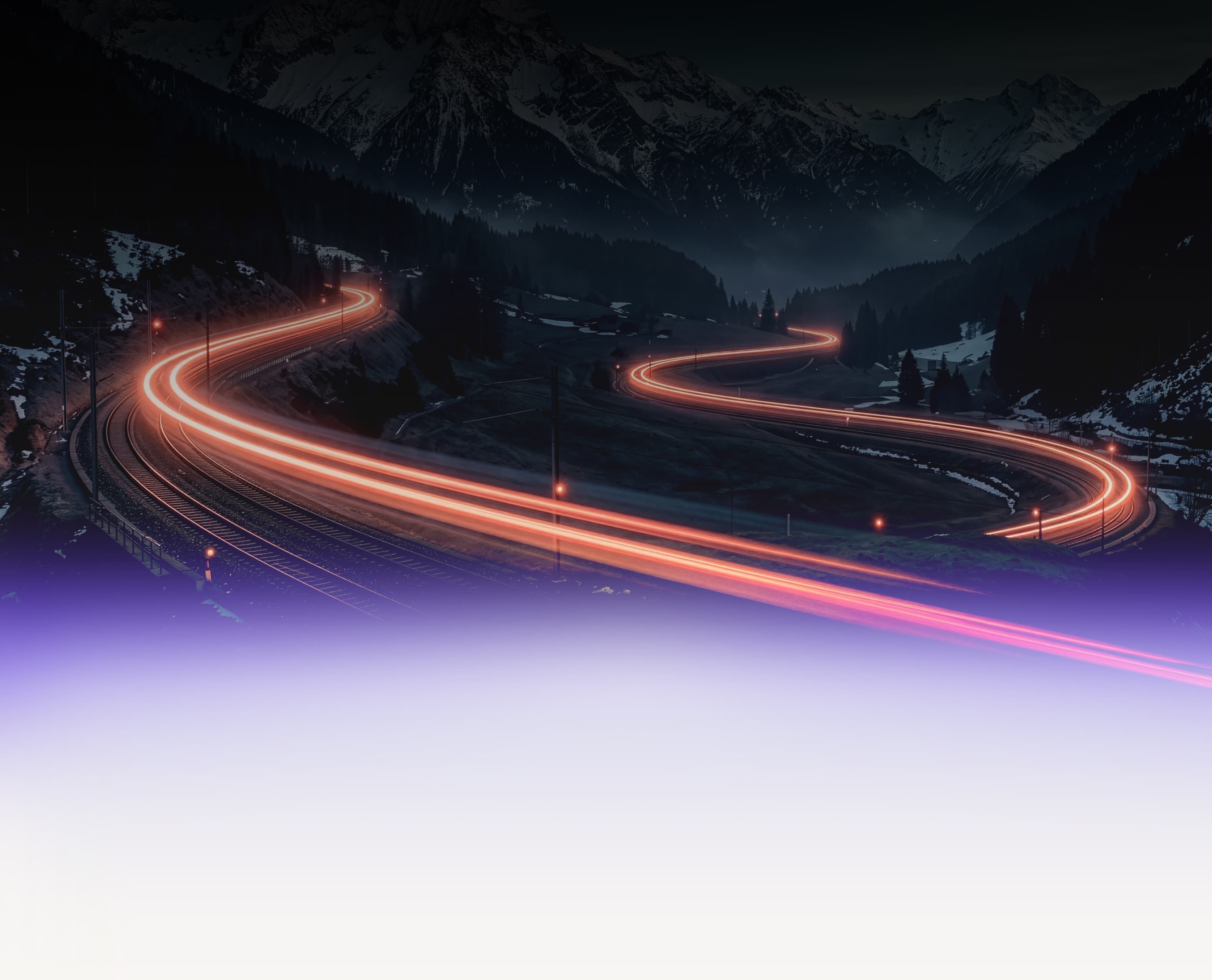A rail line winding through mountains at night, with light trails from passing trains
